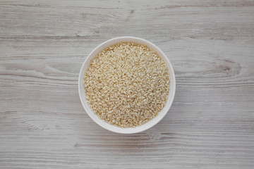 Organic Arborio rice in a white bowl on a white wooden background, top view. Flat lay, overhead, from above.