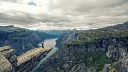 Young man climber in red jacket making intrepid handstand at the edge of famous Troltunga cliff...