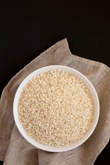 Organic Arborio rice in a white bowl on a black surface, top view. Flat lay, overhead, from above. Copy space.