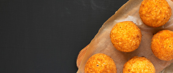 Homemade fried Arancini on a rustic wooden board on a black background, top view. Italian rice...