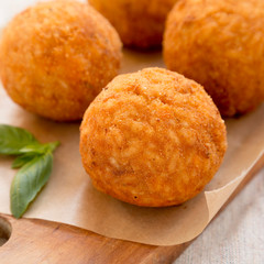 Homemade fried Arancini with basil on a rustic wooden board, side view. Italian rice balls. Close-up.
