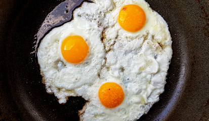 Three free range fried eggs in a hot non stick frying pan
