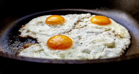 Three free range fried eggs in a hot non stick frying pan