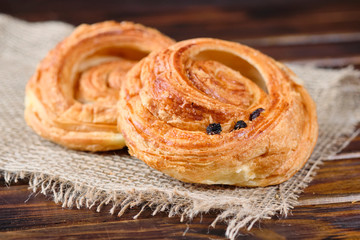 puff buns with jam and raisins in the shape of a snail on burlap and wooden background. Close-up