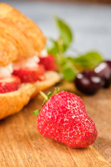 croissant sweet sandwich with cream cheese and strawberries on a wooden board and gray background. Useful breakfast. Proper nutrition. French traditional dishes.