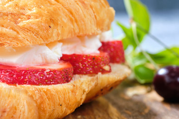 croissant sweet sandwich with cream cheese and strawberries on a wooden board and gray background. Useful breakfast. Proper nutrition. French traditional dishes.