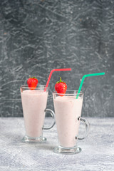 Two glasses with strawberry milkshake with pieces of berries on the edge of the glass on gray background.