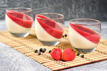 creamy panakota with strawberry jam in a glass cup on a gray background. Close-up