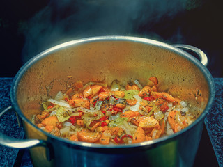 Various vegetables are cooked in a large metal pan. Steam rises above the dish.