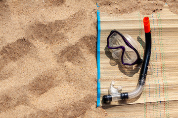 The snorkel and mask are on the beach mat by the sea.