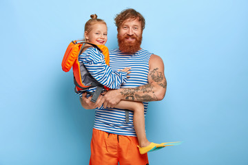 Happy affectionate father carries small daughter on hands who wears protective lifejacket and...