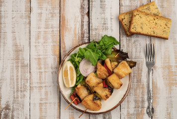 Skewed sole fish served with salad and corn bread on table