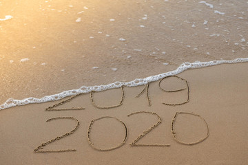 Inscription 2019 and 2020 on beach sand, wave covering 2019 digits. New Year 2020 coming concept