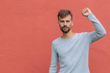 Fist of guy arm raising up showing power strong. Hand over red wall with copy space. Protest...