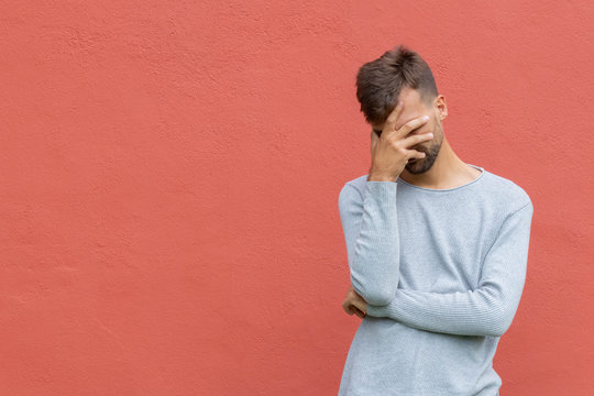 Stressed disappointed young guy making facepalm gesture with hand. Red wall background, copy space. Facepalm concept.