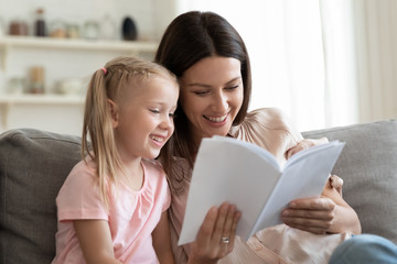 Cheerful mother and daughter sitting on couch reading fairytale
