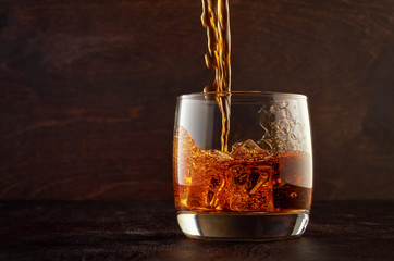 A glass of whiskey on the rocks with a double portion is on the wooden table. Top in a glass filled with whiskey.