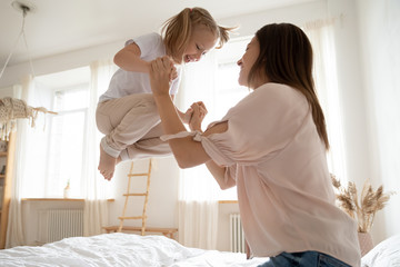Active little girl jumping in bed holding mother hands