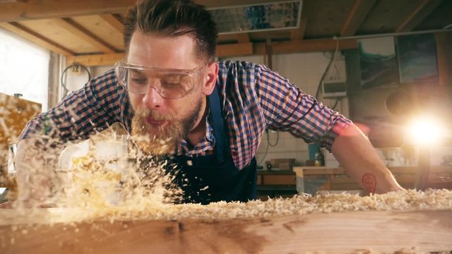 Wood shavings are getting blown off by the craftsman in slow motion
