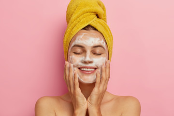 Morning routine and relaxing time concept. Pleased young woman washes face, cleans skin with soap,...