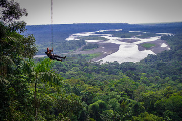 Tourist having fun in the air held by a rope. Fabulous Amazonian landscape where you can appreciate...