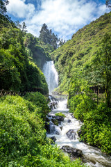 View of Peguche Waterfall in the mountains of Ecuador. There is a huge waterfall surrounded by a lot of vegetation