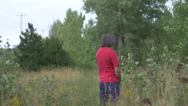 Man urinating in nature in a field during summer.