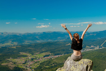 The girl at the top of the mountain raised her hands up. Wide summer mountain view at sunrise and distant mountain range covered. Beauty of nature concept