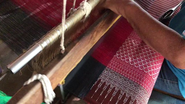 Hands of old woman weaving on a loom or weave lag with weaving machine, A traditional hand-weaving loom being used to make cloth at home in the north of Thailand. working concept. 4K video footage.