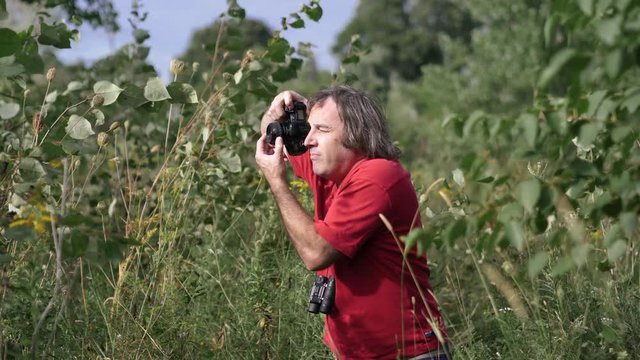 Photographer with DSLR camera and binoculars taking pictures in nature