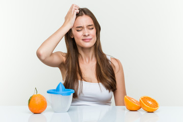 Young caucasian woman with an orange juicer being shocked, she has remembered important meeting.