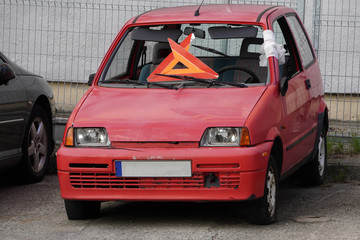 Fototapeta na wymiar broken old car coral color is in the yard. emergency stop sign instead of windshield, front strut wrapped with duct tape