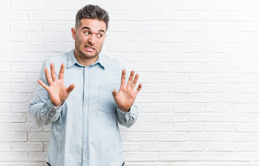 Young handsome man against a bricks wall rejecting someone showing a gesture of disgust.