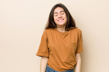 Young brunette woman against a beige background laughs and closes eyes, feels relaxed and happy.