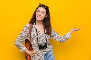 Young brunette traveler woman showing a copy space on a palm and holding another hand on waist.