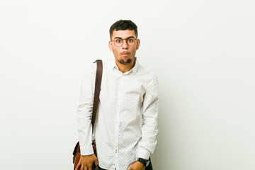Young hispanic casual business man shrugs shoulders and open eyes confused.