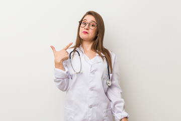 Young doctor woman against a white wall pointing with finger at you as if inviting come closer.