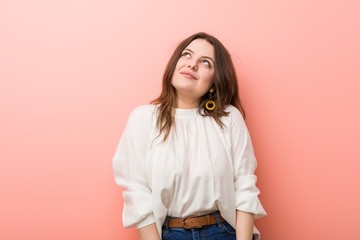 Young caucasian curvy woman standing against pink background