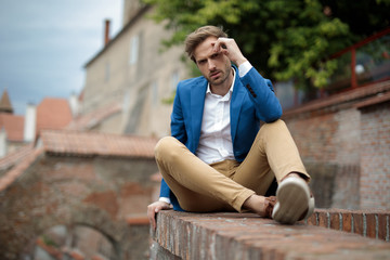 Fototapeta premium pensive fashion man sitting on brick wall and rests