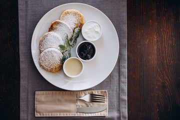 Delicious and hearty dessert, home made cottage cheese fried in a pan and served with sauces. Cheesecake, fresh jam and mint. Cottage cheese pancakes or curd fritters decorated powdered sugar in plate