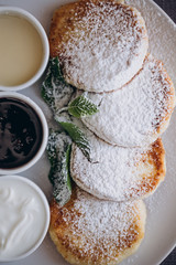 Delicious and hearty dessert, home made cottage cheese fried in a pan and served with sauces. Cheesecake, fresh jam and mint. Cottage cheese pancakes or curd fritters decorated powdered sugar in plate