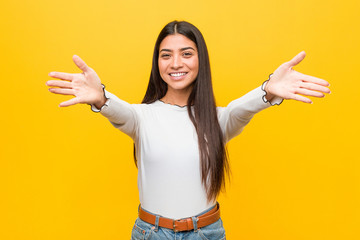 Young pretty arab woman against a yellow background feels confident giving a hug to the camera.