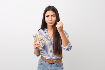 Young arab woman holding dollars showing fist to camera, aggressive facial expression.