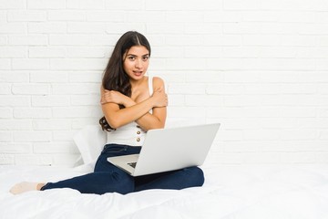 Young arab woman working with her laptop on the bed going cold due to low temperature or a sickness.