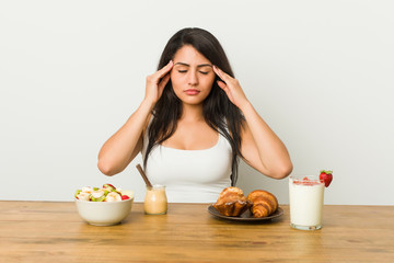 Obraz na płótnie Canvas Young curvy woman taking a breakfast touching temples and having headache.