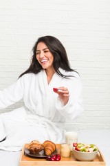 Young hispanic woman having breakfast on the bed