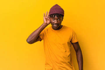 Young black man wearing rastas over yellow background trying to listening a gossip.