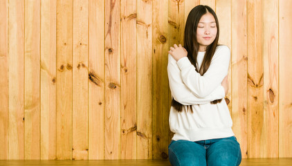 Fototapeta premium Young chinese woman sitting on a wooden place hugs, smiling carefree and happy.