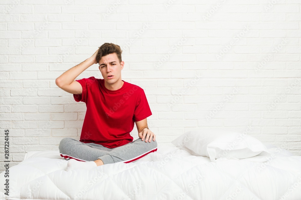 Wall mural Young teenager student man on the bed tired and very sleepy keeping hand on head.