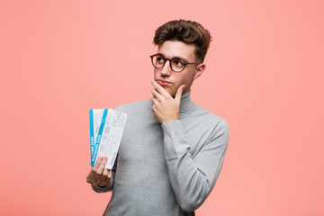 Young cool man holding an air tickets looking sideways with doubtful and skeptical expression.